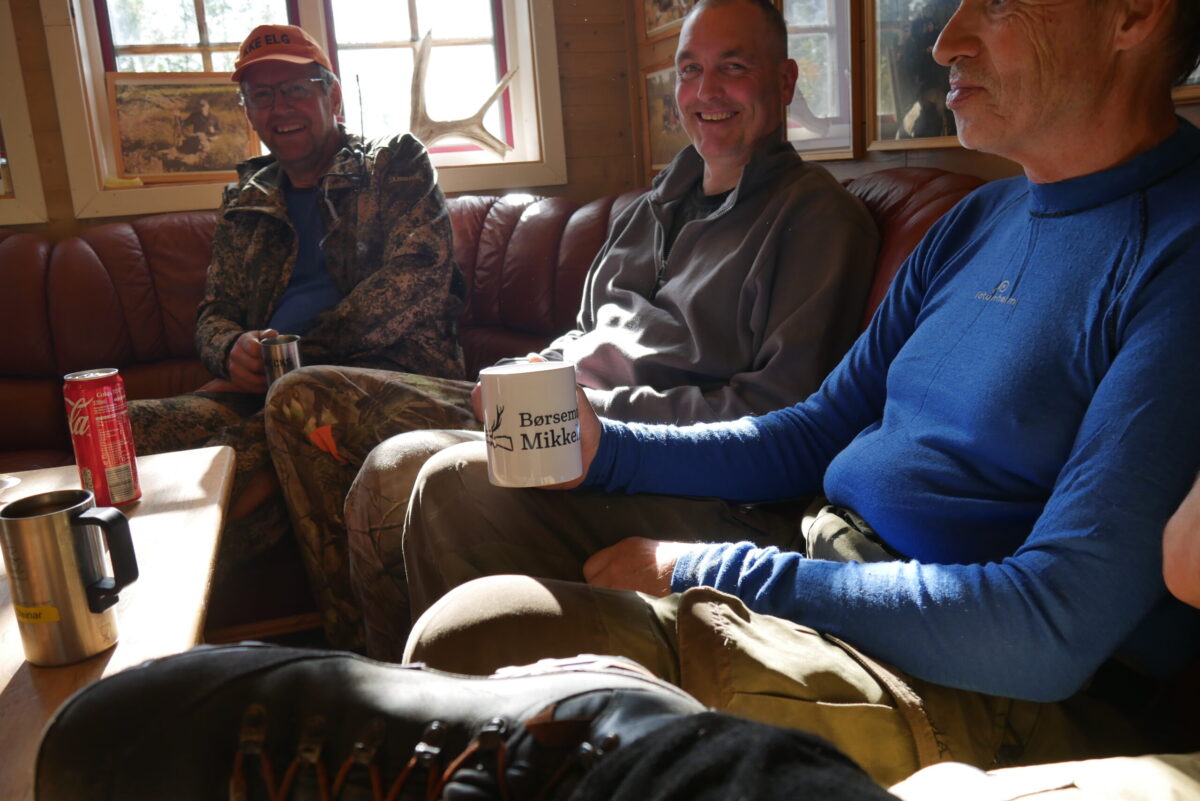 Bilde av deler av jaktlaget over kaffekopp i sofaen i jakthytta.