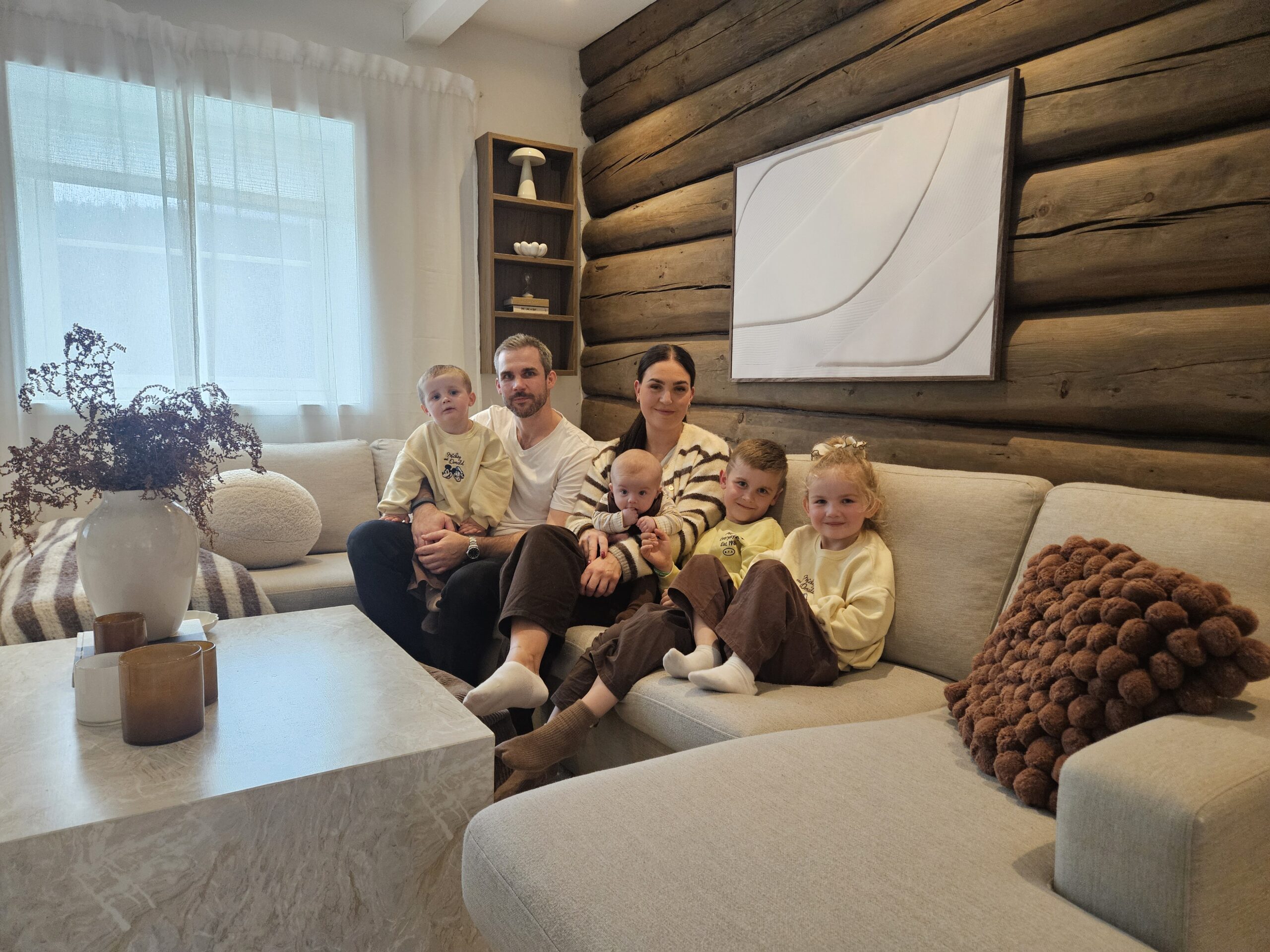 Familie på to voksne og fire barn i en sofakrok i en lys og trivelig stue.